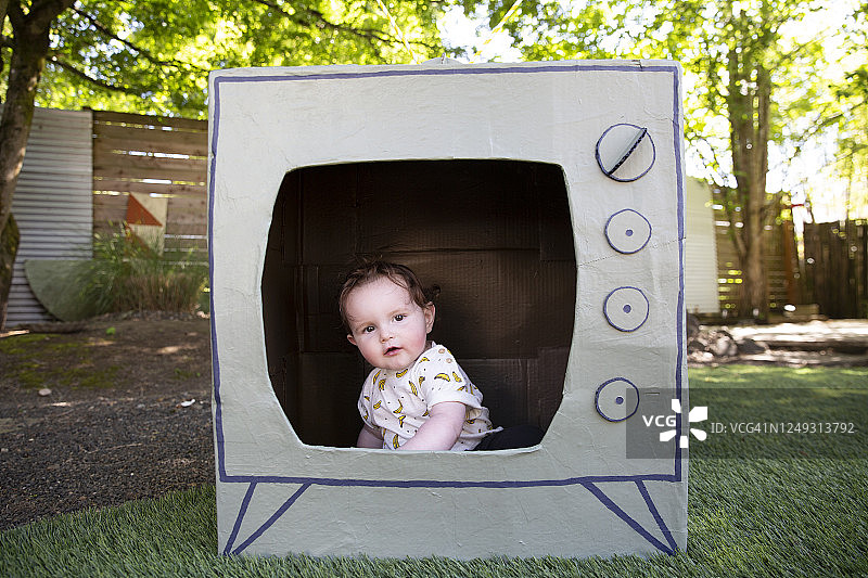 坐在纸盒电视机里，调皮地看着镜头外的婴儿图片素材