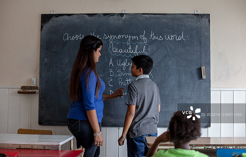 女老师在课堂上把粉笔递给小男孩，让他回答黑板上的问题图片素材