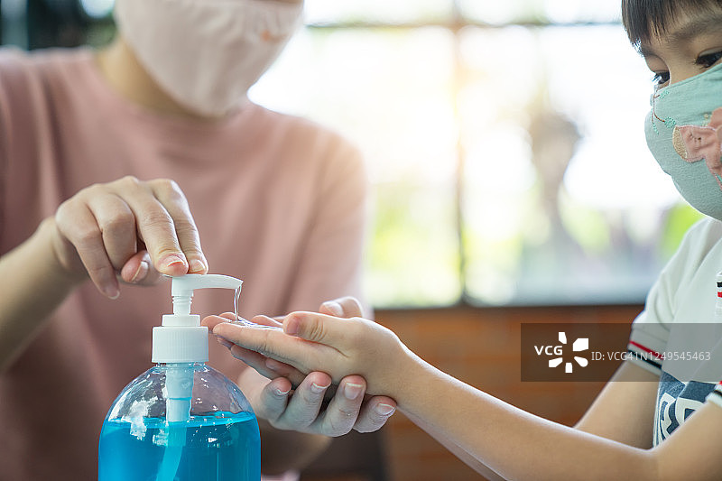 年轻妈妈给小儿子的手上挤洗手液，以防止病毒传播图片素材