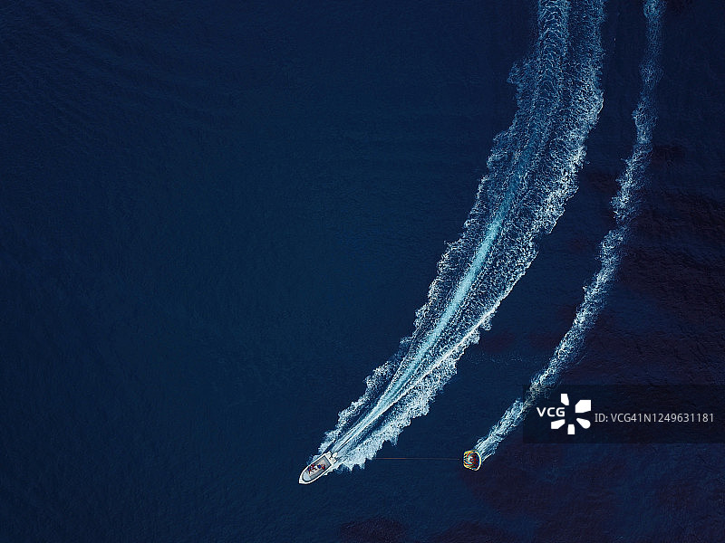 夏季水上运动：海滩上快艇拖拽充气游乐设施的航拍视角图片素材