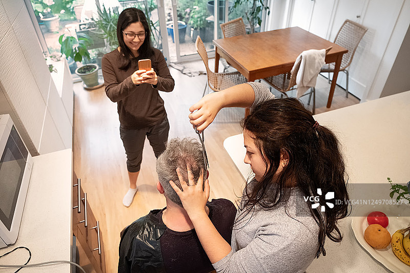 少女给父亲理发，妹妹用手机拍摄图片素材