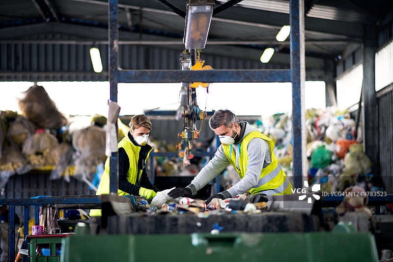 戴着防护口罩的男女工人在垃圾填埋场，废物管理和环境概念图片素材