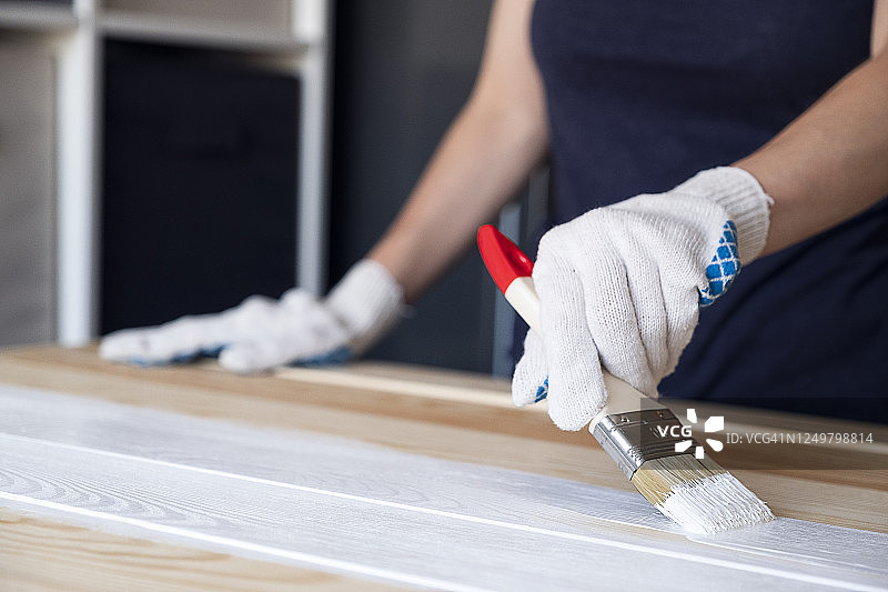 戴防护手套的女人用白色油漆刷。绘画和维修工作。女人粉刷木板、桌子和表面，自己制作木制摄影板。图片素材