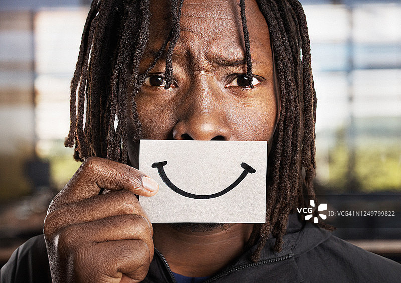 悲伤焦虑的男人拿着微笑卡片遮住嘴巴图片素材