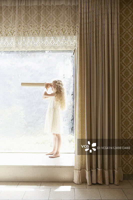 站在窗台上，用纸板望远镜向外看的女孩图片素材