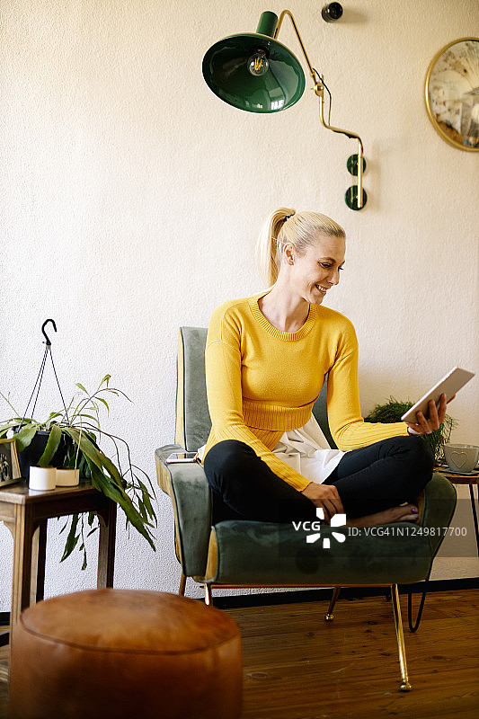 微笑的金发女子坐在家中的扶手椅上使用数位板图片素材