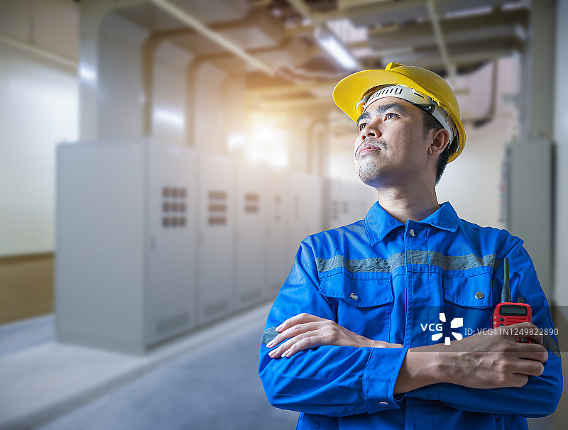 身穿制服和黄色头盔的年轻电气工程师在开关设备电气室手持无线电通讯设备图片素材