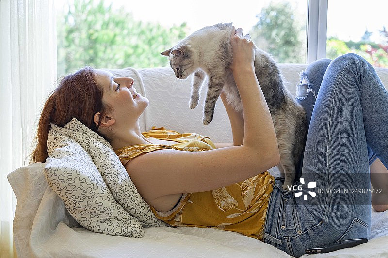在家躺在沙发上抱着猫的年轻女人图片素材