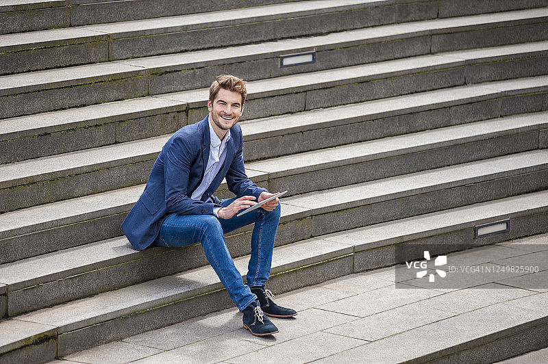 快乐的年轻商人坐在楼梯上使用平板电脑图片素材