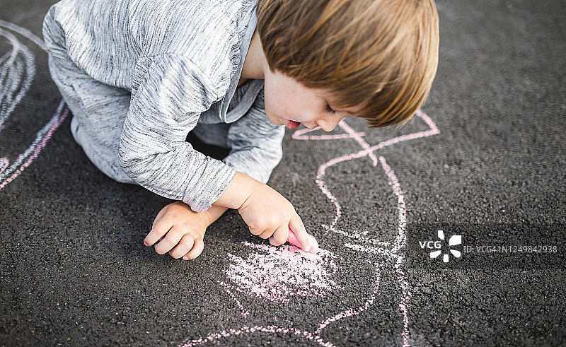 小男孩用粉笔在柏油路面涂鸦图片素材