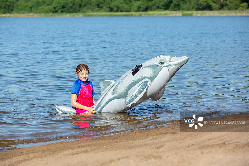 坐在海滩充气海豚玩具上的女孩图片素材