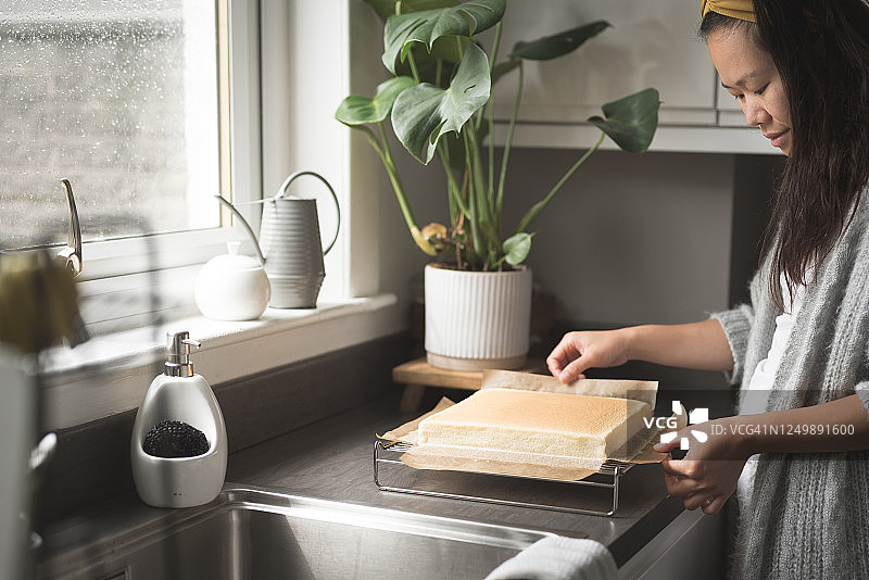亚洲女人从方形海绵蛋糕上取下烘焙纸图片素材