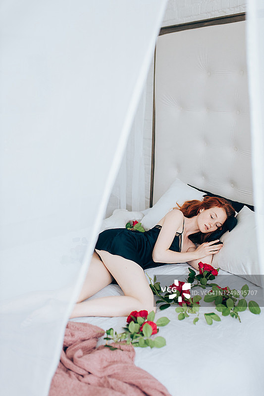 年轻的红发女人躺在铺满玫瑰的床上图片素材