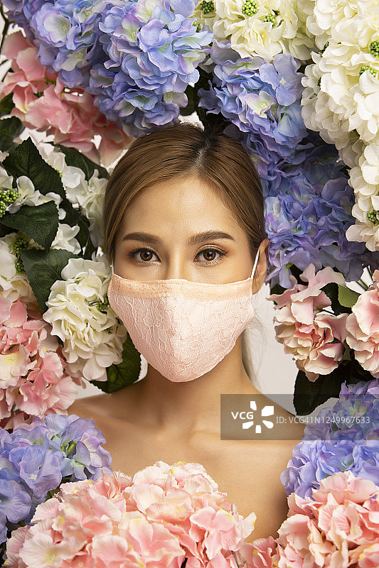 戴口罩的亚洲女性美丽竖版肖像，绽放鲜花背景，放松微笑图片素材