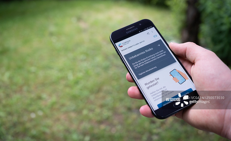 男人手持安卓智能手机，屏幕上显示德国官方的“新冠预警App”图片素材