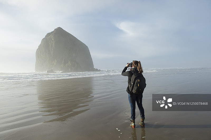 女人在俄勒冈州坎农海滩拍摄干草堆岩的背影图片素材