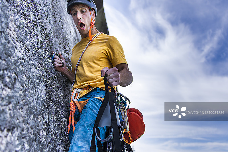 攀岩者在墙上拿着露营吊床，面部表情滑稽，张着嘴图片素材