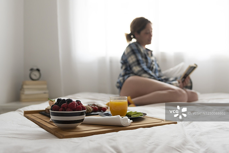 专注的早餐托盘和在背景中阅读的模糊女人图片素材