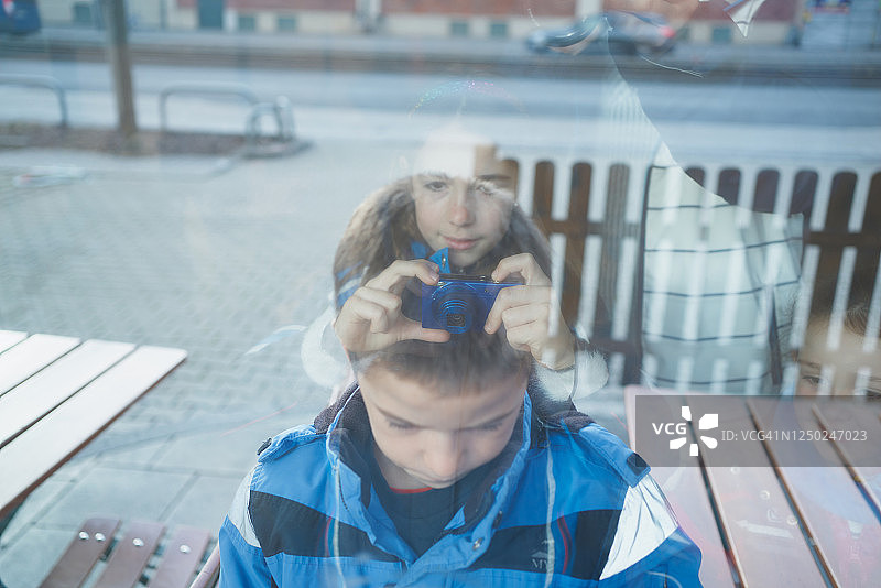 女孩拍摄玻璃后面的男孩图片素材