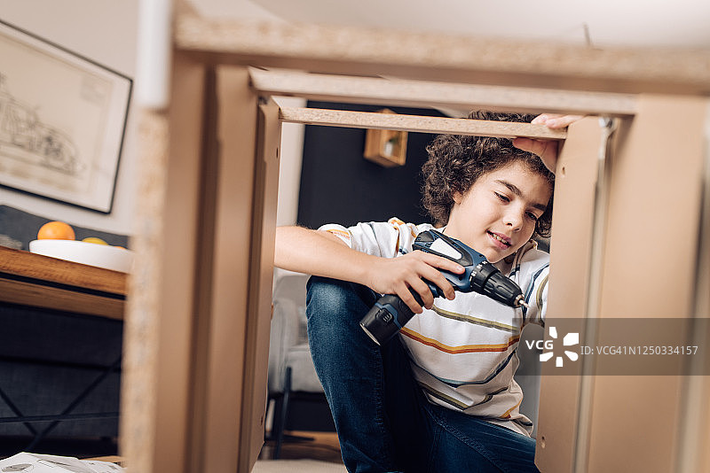 男孩在家用电动螺丝刀组装木桌图片素材