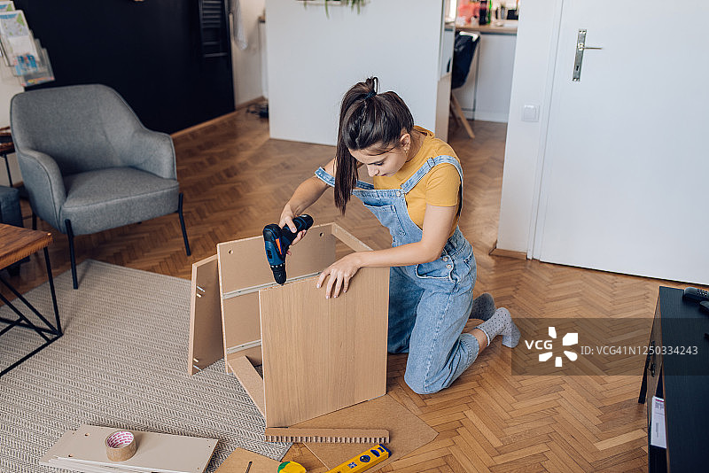 使用电动螺丝刀安装新书架的少女图片素材