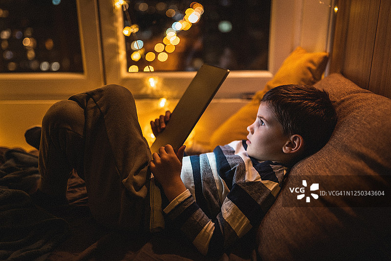 可爱的小男孩躺在床上用平板电脑看书图片素材