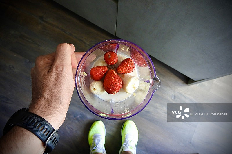 跑步后，搅拌机中准备搅拌的草莓、香蕉和豆奶，在男人手中图片素材