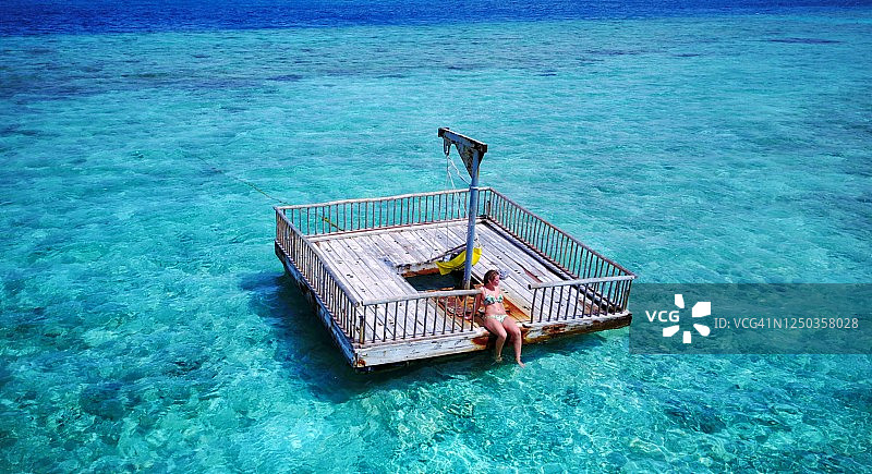 年轻女人坐在蓝色泻湖中的木筏上，沐浴阳光图片素材
