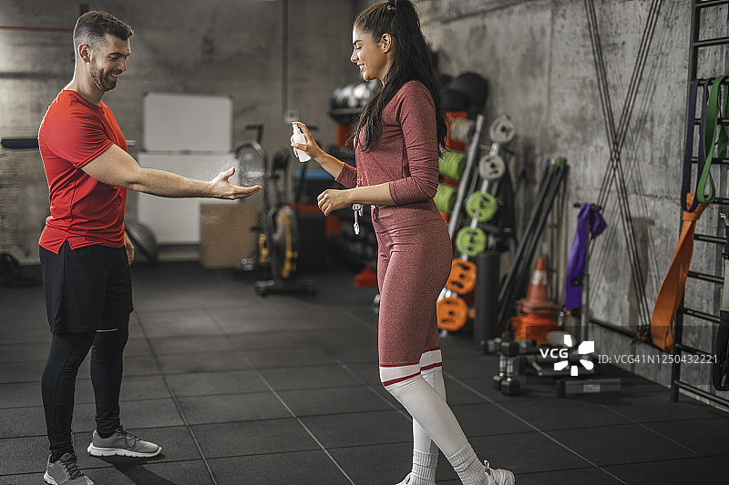 运动后，运动型女人将消毒洗手液喷洒到男人手上图片素材