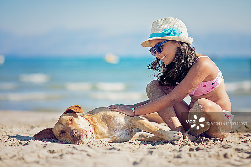 小女孩在海滩上抚摸着她熟睡的狗图片素材