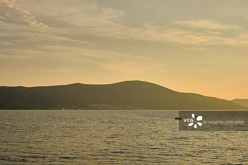 日落时分，山景背景下的游艇与小船，天空中漂浮着云朵，飞机划过天际图片素材