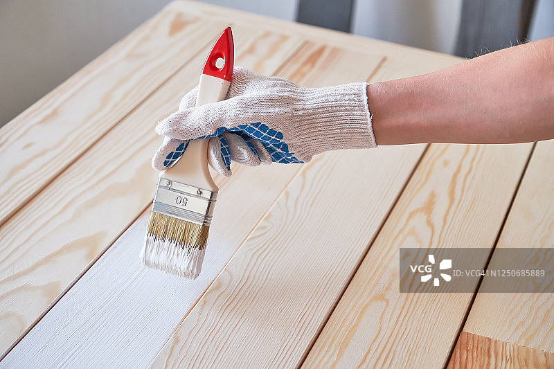 戴防护手套的女人用白色油漆刷。油漆和维修工作。女人粉刷木板和表面，自己制作木制摄影板。图片素材