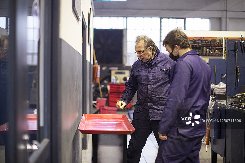 一位年长的男人向年轻的实习生讲解发动机部件图片素材