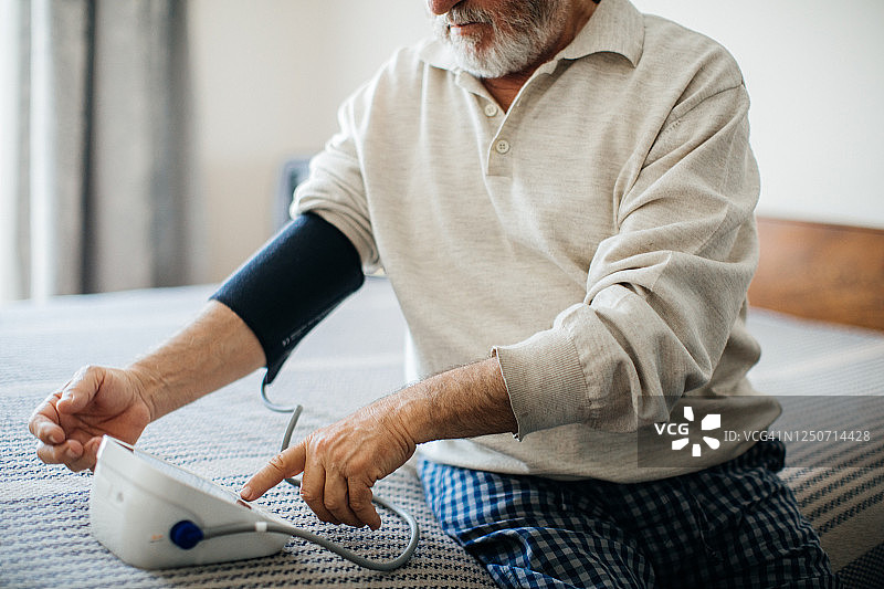 年长的男人在卧室里用血压计测量血压图片素材