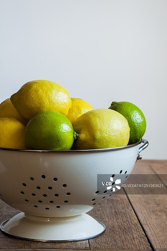 木桌上滤器中柠檬和酸橙的裁剪图像，浅色背景图片素材