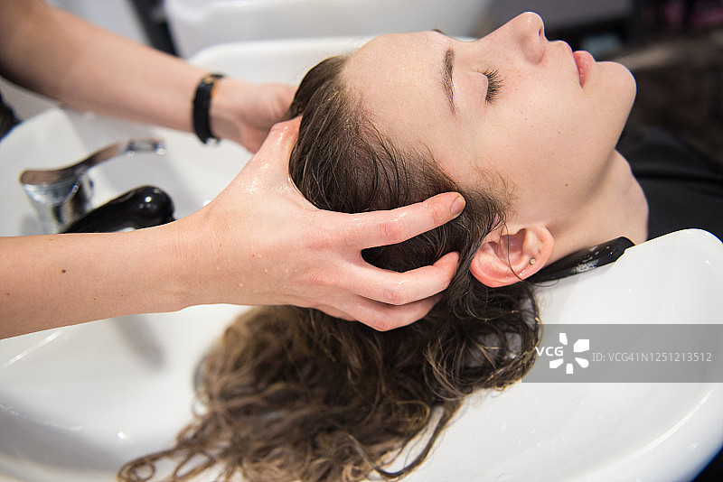 年轻女人在美发沙龙洗头时享受头部按摩图片素材