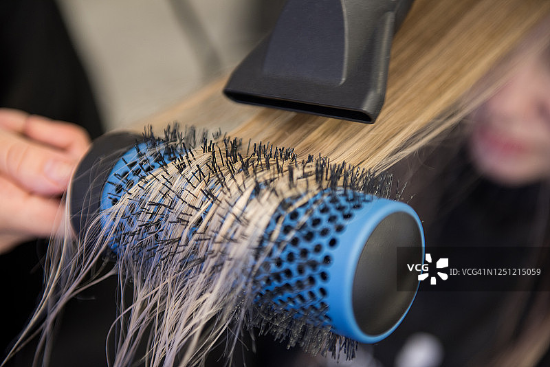 在美发沙龙用发刷和吹风机拉直头发特写图片素材