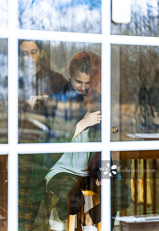 从后门廊透过玻璃门看客厅里姐姐给妹妹剪头发图片素材