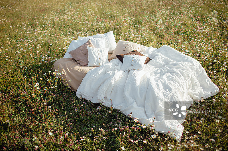 夏季洋甘菊田野中铺着白色床单的舒适床铺。夏季度假灵感，良好睡眠和放松的概念。图片素材