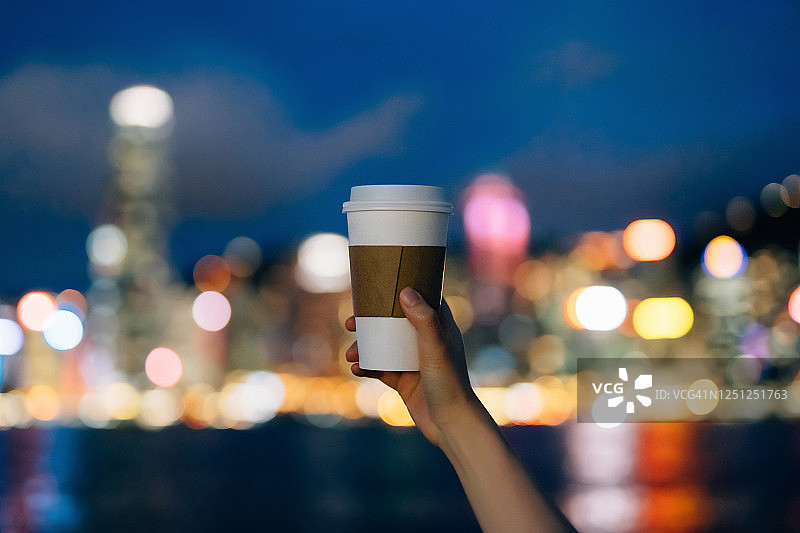 女子手拿咖啡，背景是城市夜景灯光图片素材