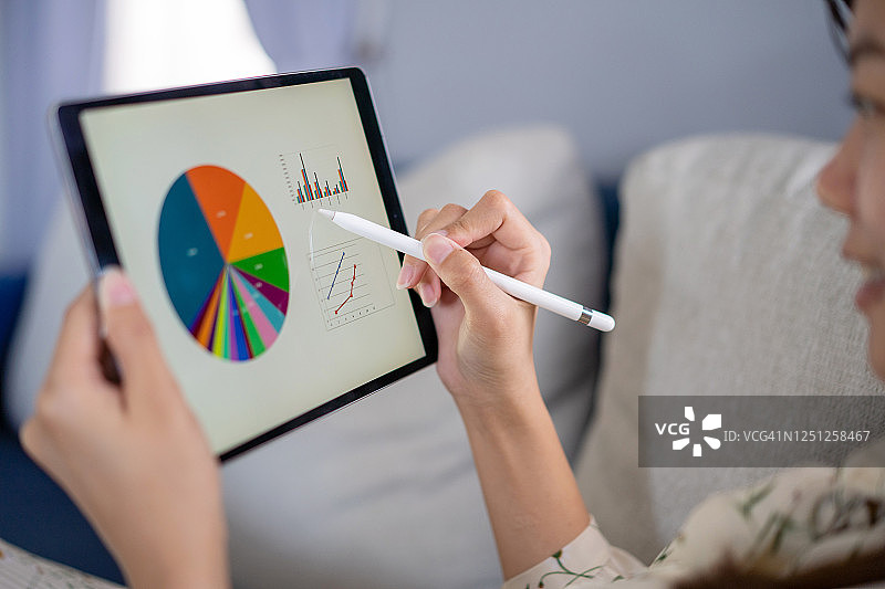 年轻亚洲女性坐在沙发上，使用平板电脑和手写笔工作图片素材