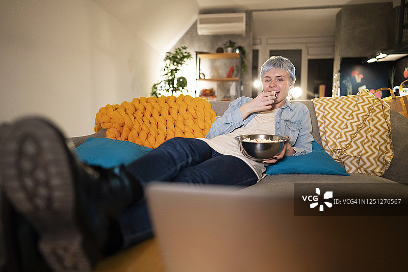年轻白人女子在家里看电影，吃着爆米花图片素材