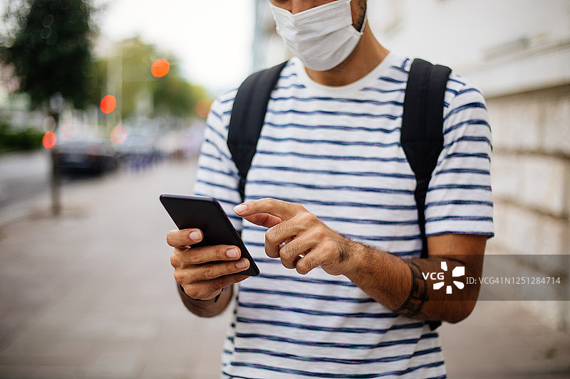 男人戴口罩在街上使用手机的肖像图片素材