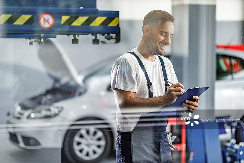 快乐的机修工在汽车修理店里做笔记图片素材
