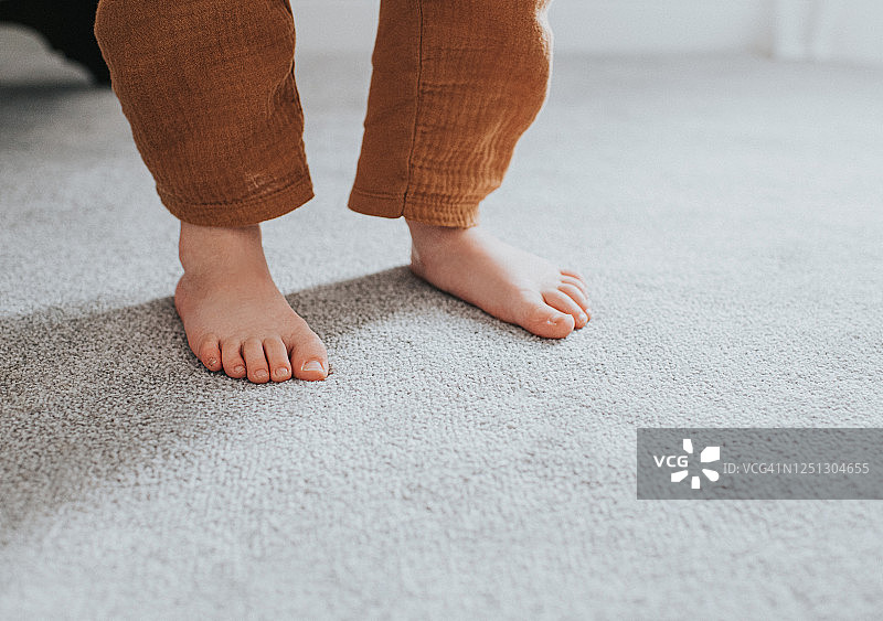 灰色厚绒地毯上儿童的脚，投下阴影图片素材