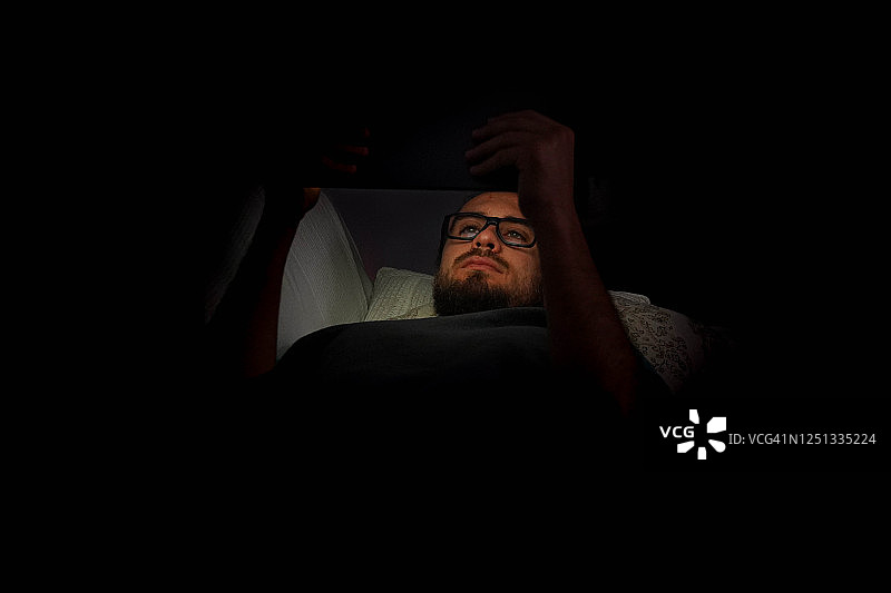 男子夜晚在沙发上使用平板电脑图片素材