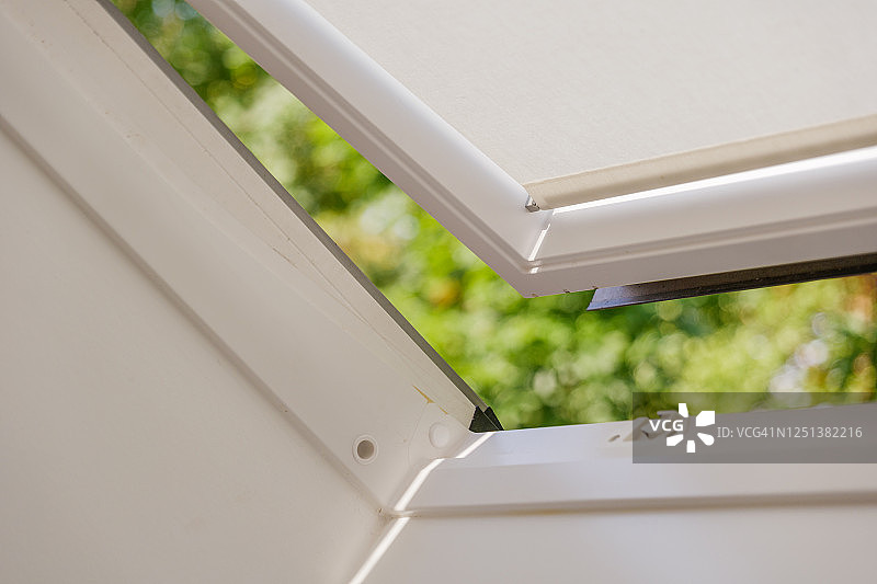 阁楼带窗帘的白色倾斜天窗特写，户外绿色散景虚化图片素材