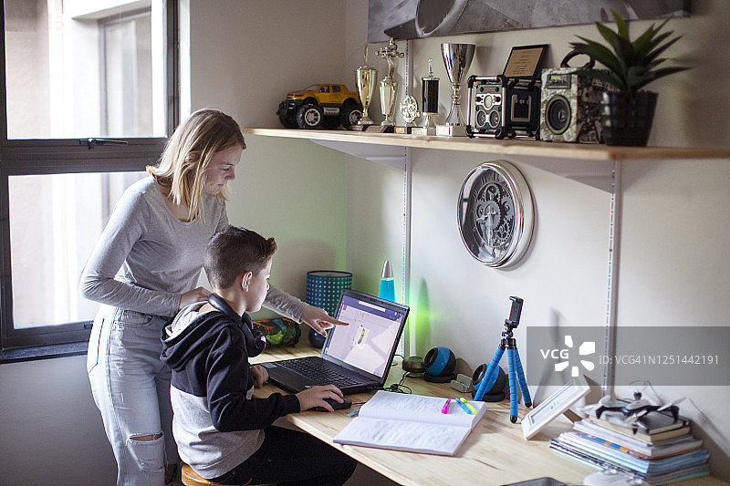 姐姐在家帮助弟弟用笔记本电脑完成学校作业图片素材