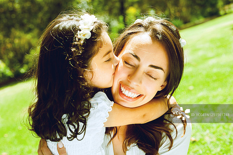 可爱的女儿在公园里拥抱亲吻妈妈的脸颊图片素材