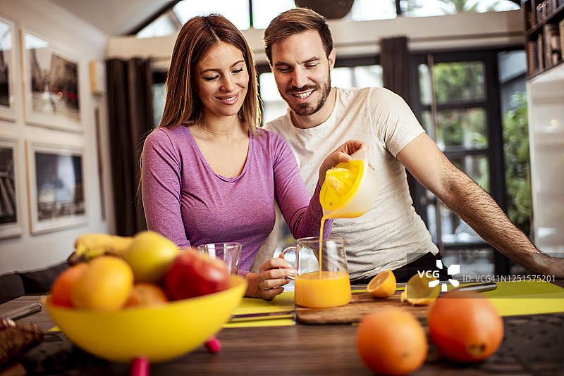清晨，年轻女人与伴侣在餐厅倒橙汁图片素材